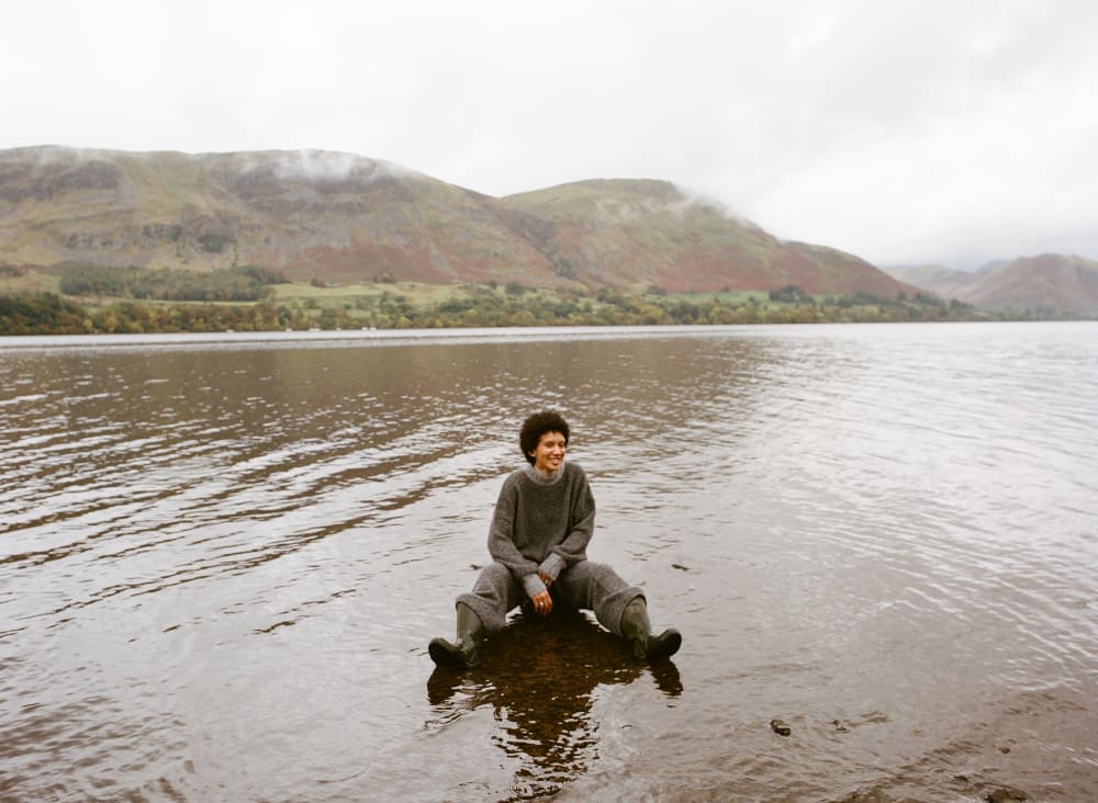 Woman sitting in shallow lake with hills in the background