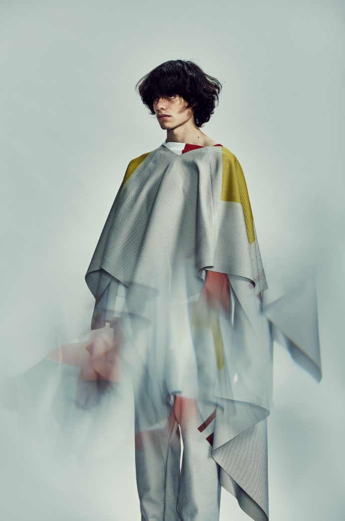 Person standing in grey clothing against grey background. Blurred in the middle of the photo.