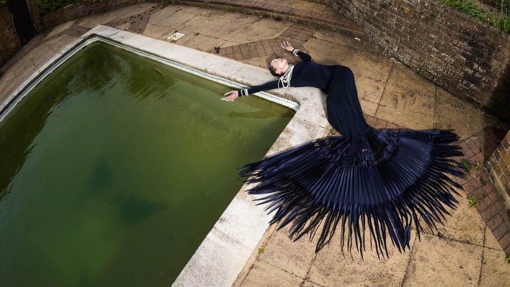 Woman lying across poolside draped in blue spikes dress