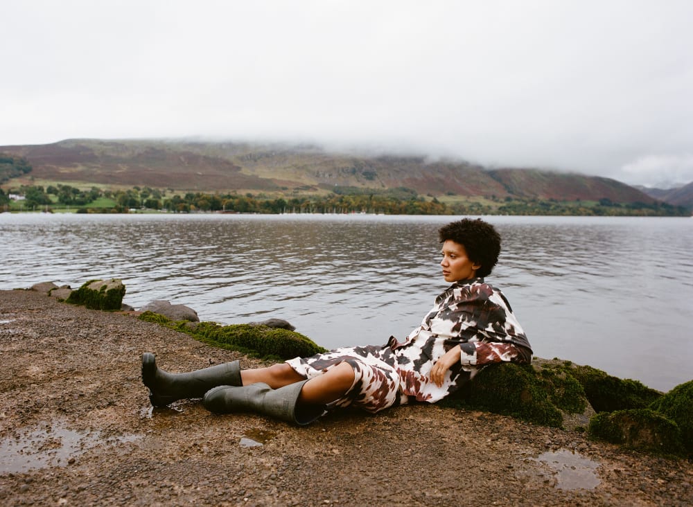 Woman laying back on the wet stoned ground with lake and hills in the background and misty white clouds