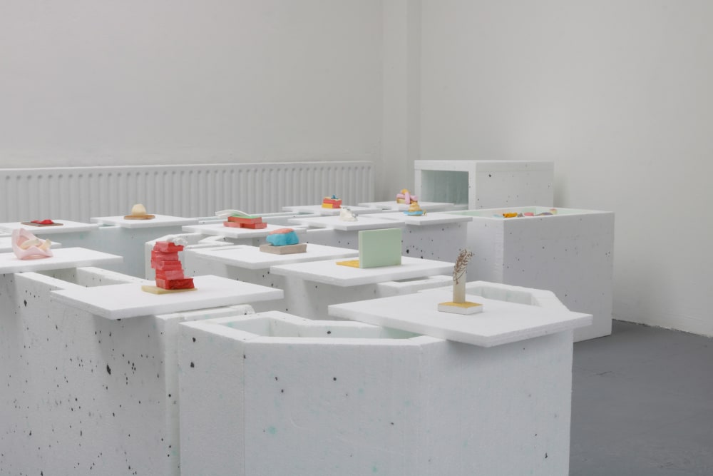 white foam board creates a conveyer belt which holds a series of brightly coloured sculptures created from a range of materials