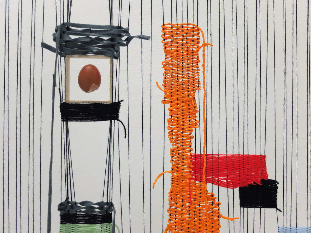 Sculptural installation created from coloured yarn and black tape, with an egg in a vitrine suspended in the middle.