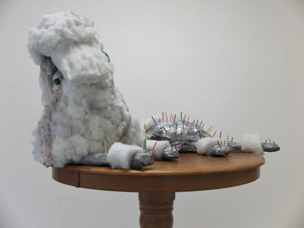 A sculpture created from various materials, including tin foil and cotton wool, suspended on a round wooden table.