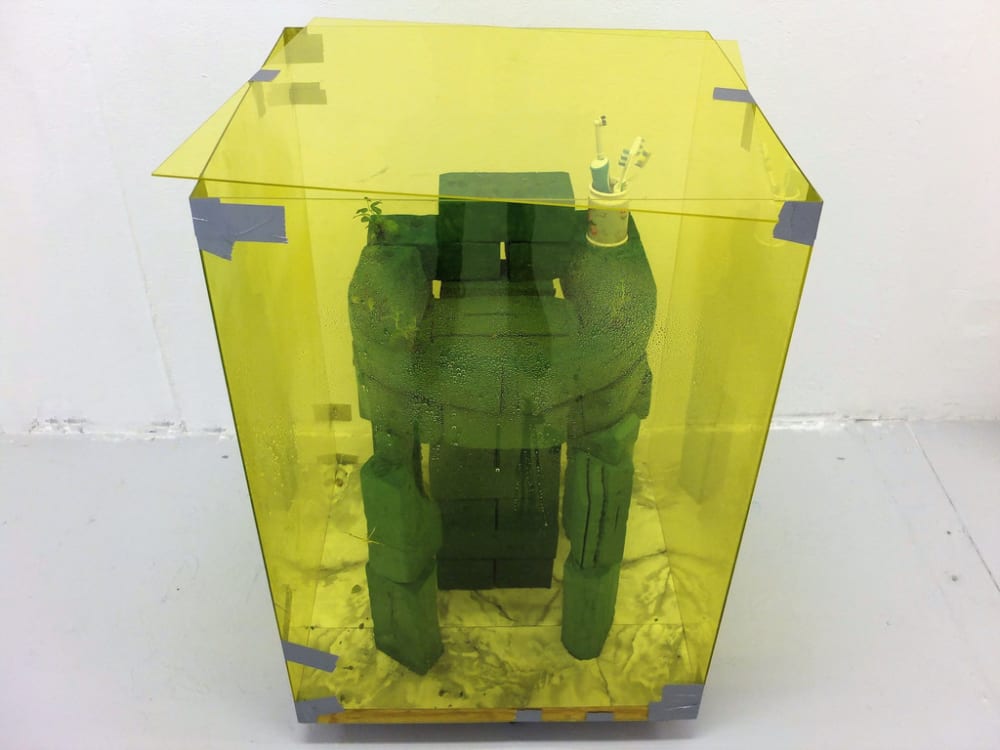 A transparent yellow vitrine containing a sculpture.