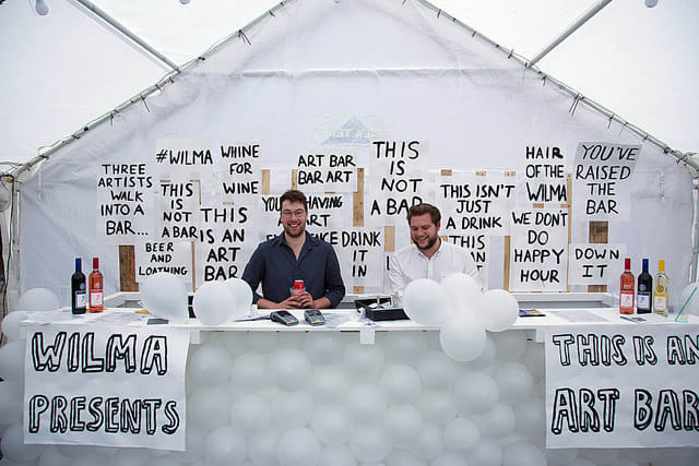 Two men sitting behind a bar at a private view.