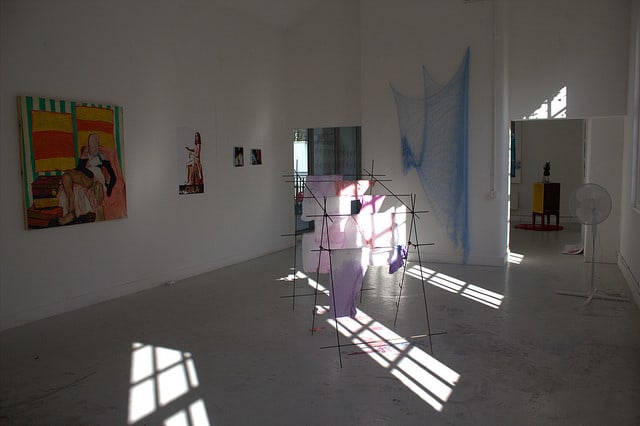 An installation in a gallery space featuring sculptures on the ground and paintings on the walls.