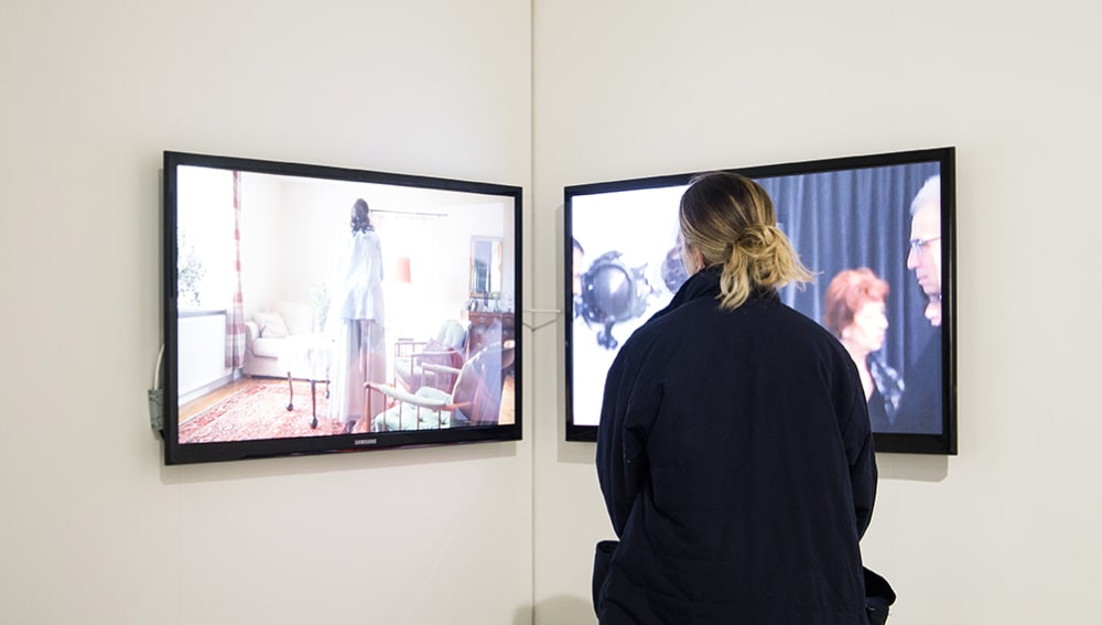 A figure looking at two video screens in a gallery