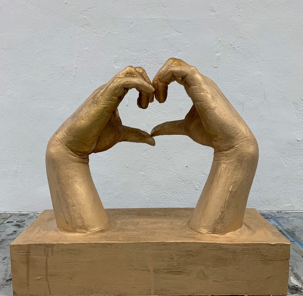 Two hands cast with bronze and gold powder on plaster. The hands are coming together to form a heart shape.