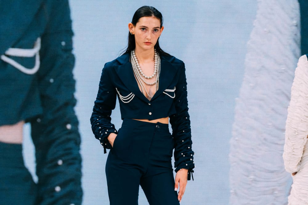 Model on stage wearing navy blue blazer and trousers