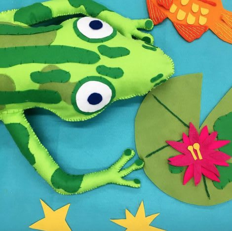 A detail of a frogs face and lily pad made from fabric.