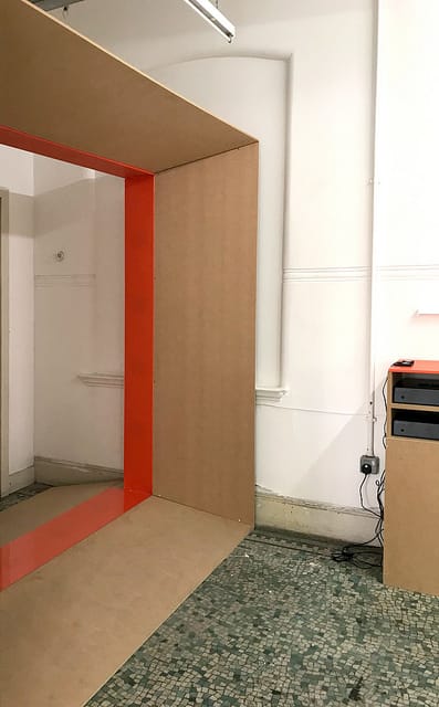 A side angle of the wooden and red box sound installation with two speakers beside it.