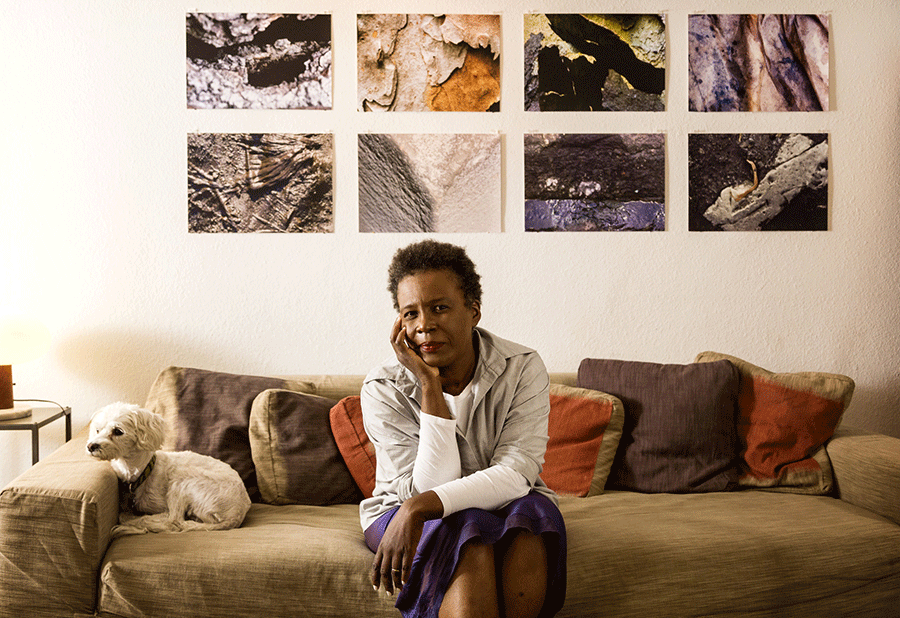 A woman sitting on a sofa next to a dog with 8 images on the wall behind her.