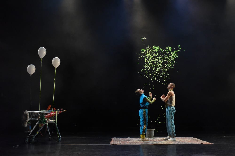 Two performers on stage with green confetti and shopping trolley