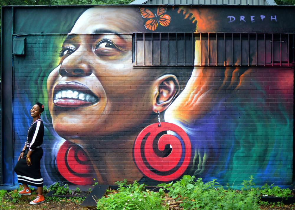 a large scale portrait mural on a wall, with the model of the portrait standing next to the painting