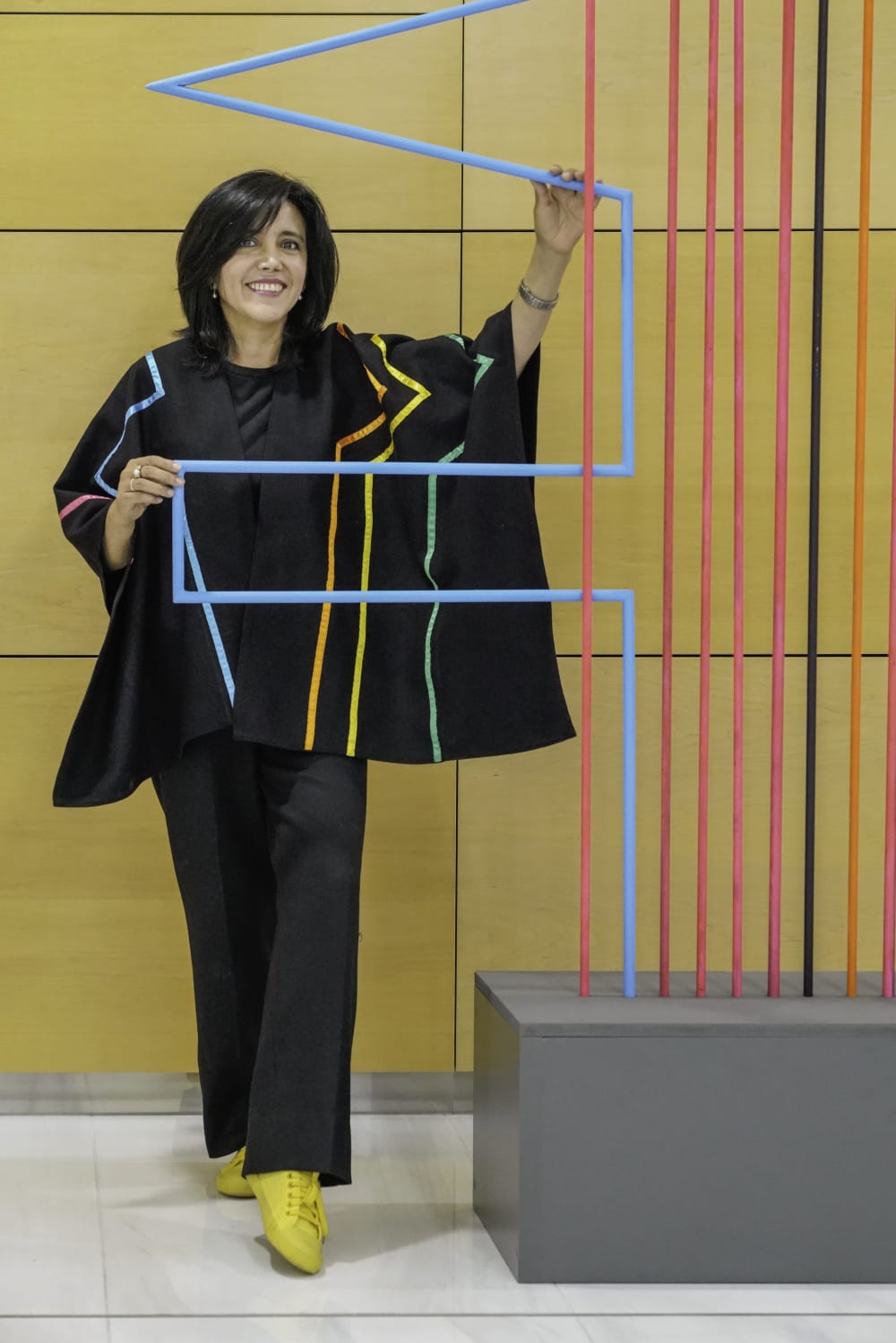 Photo of Susana standing to the left of her sculpture, against a yellow background