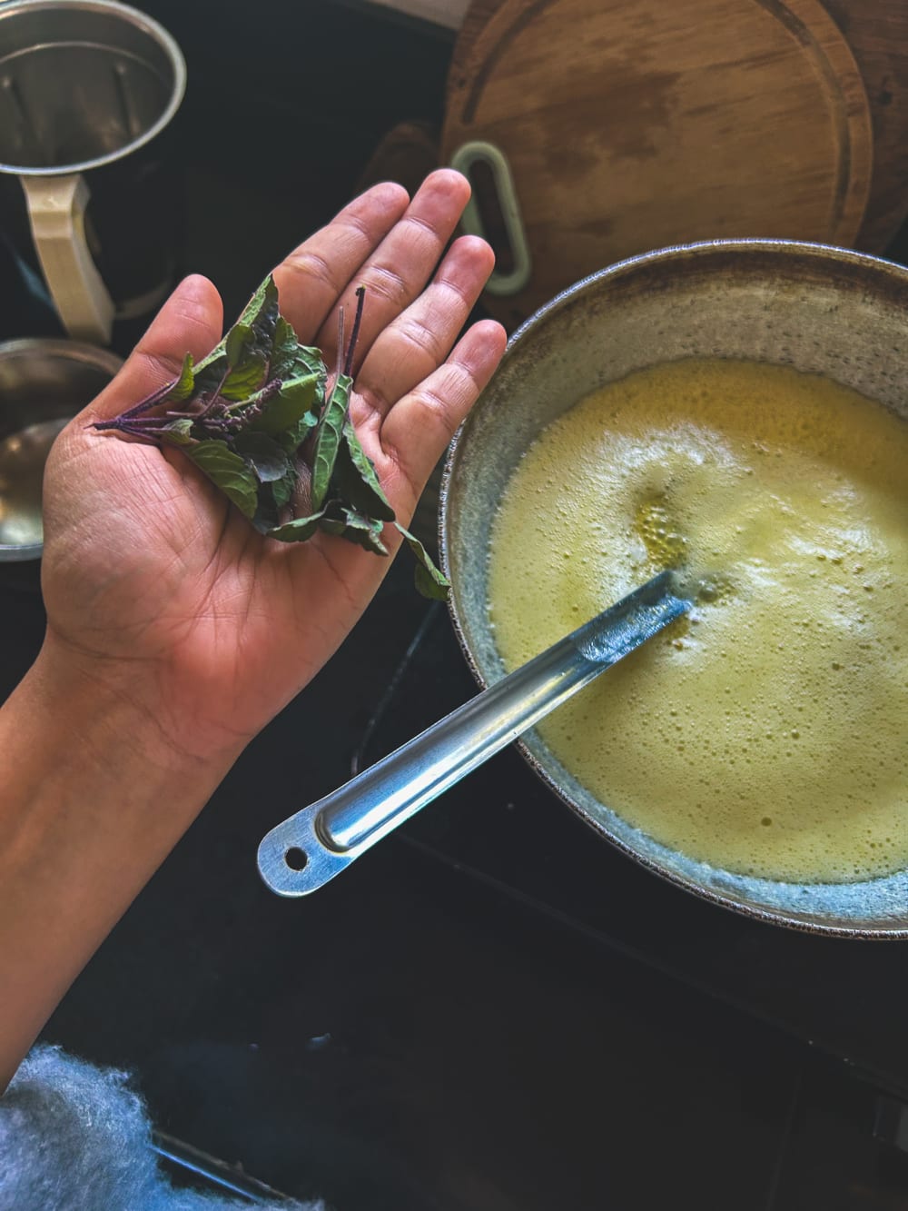 A woman's hand is holding up herbs to a bowl of ghee (clarified butter)