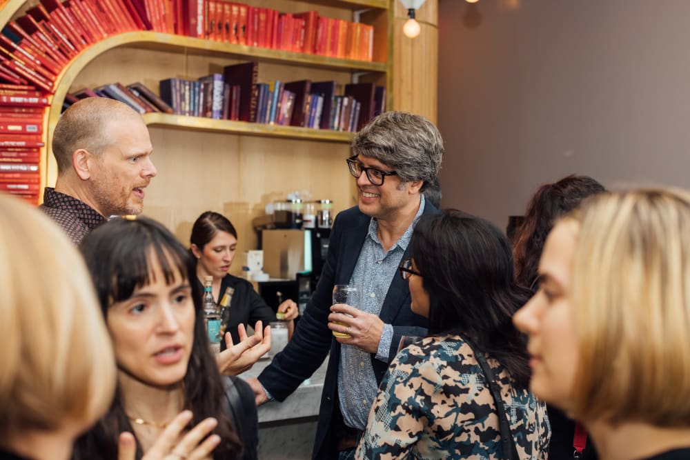 Guests chatting. In the background. 2 men standing at the bar, and in the foreground a group of women are chatting. 
