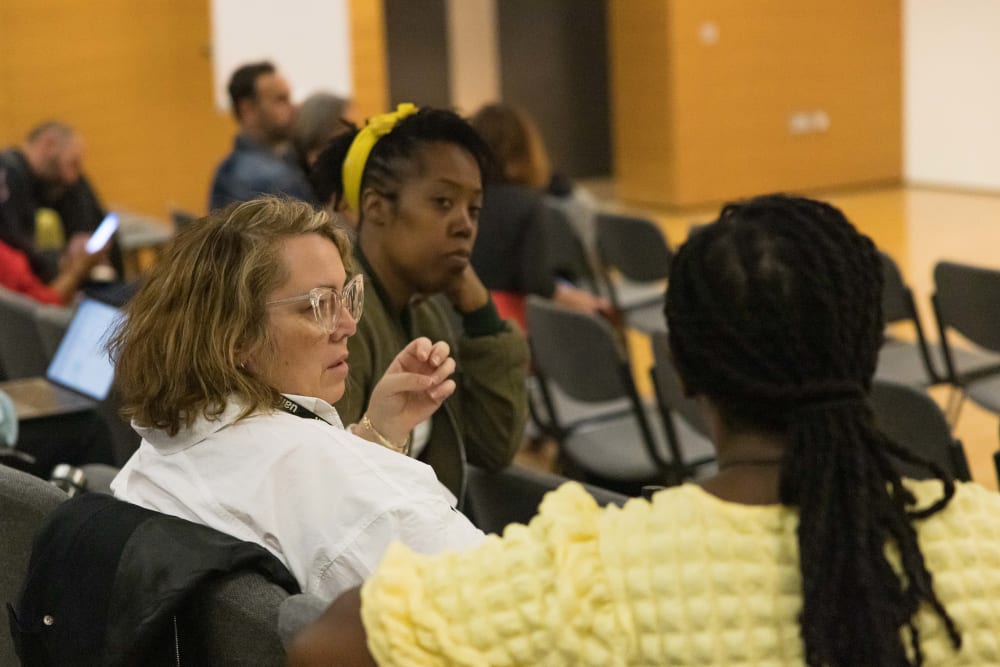 Three people sitting in lecture theatre chat amongst each other. 