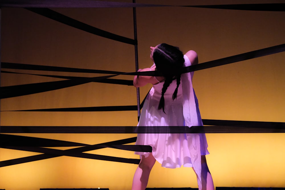 A performer in a sheer white dress with plaits and back to camera is lit in yellow and is arched backward. Behind and around them are several horizontal black bands at different heights taking up the full width of the image.
