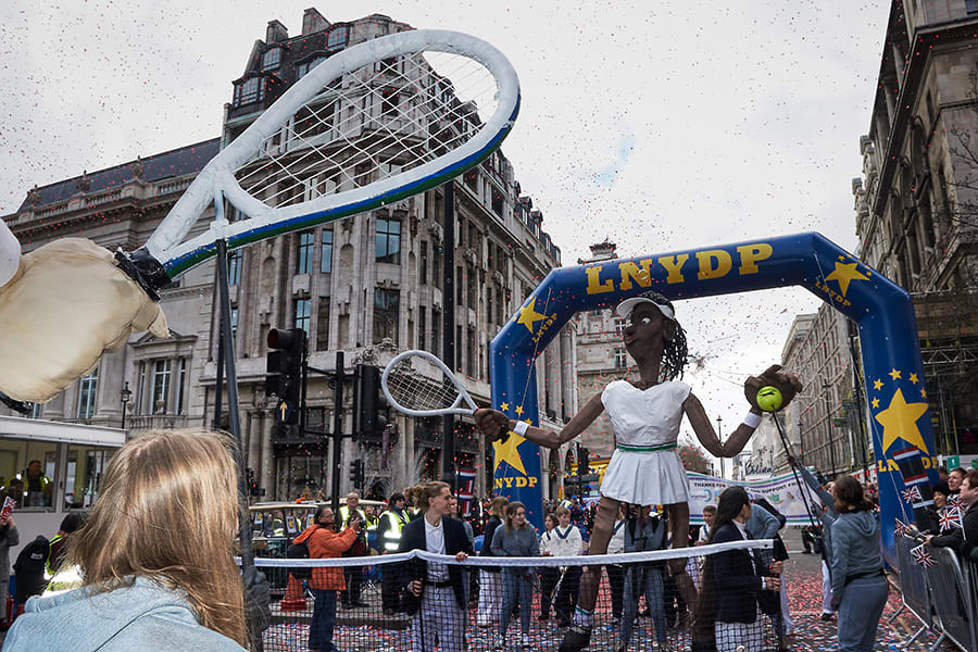 Female tennis player puppet under London New years Day Parade banner.