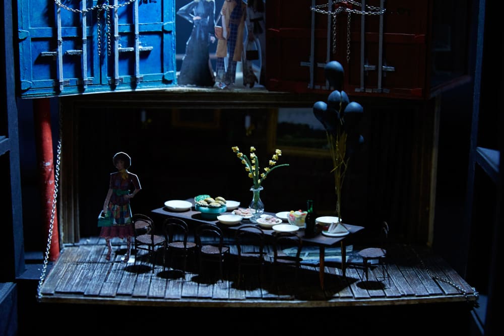 An small scale set design featuring the cutout of a woman and a table and chairs.