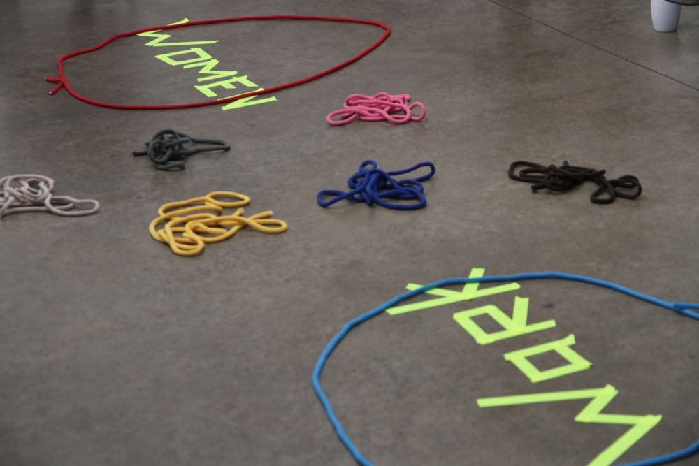 The words 'women' and 'work' written in neon yellow tape surrounded by brightly coloured string