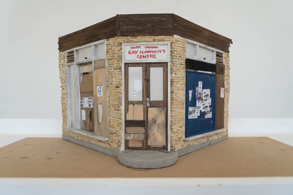 A small scale model of a shop front, boarded up, with a sign reading South London Gay Community Centre over the door.