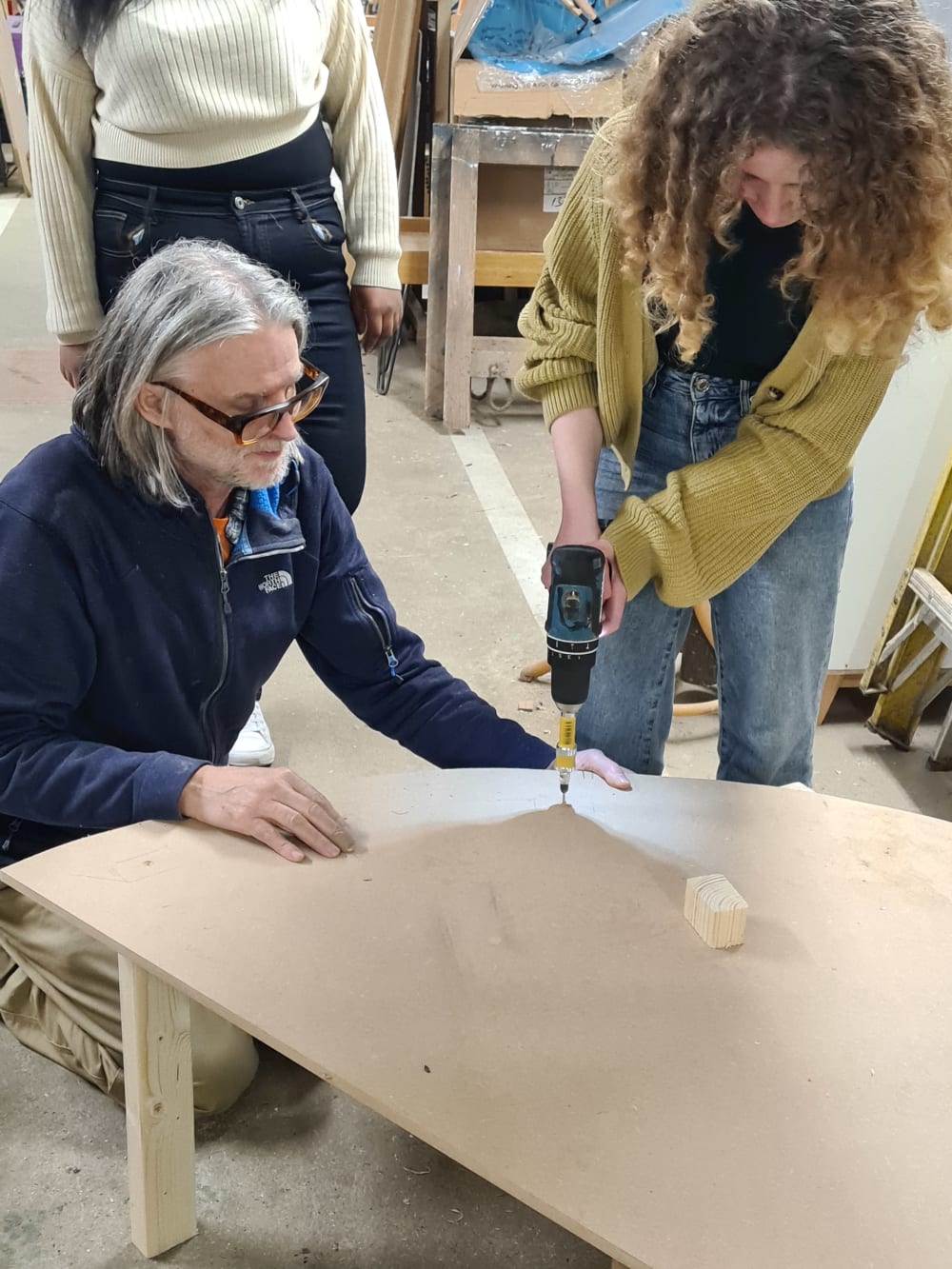 A man and a woman working together to build a table using wood and a drill