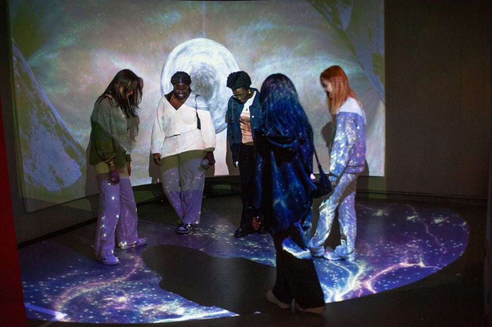 Guests exploring the work on display. A group of women surrounded by a galaxy projection