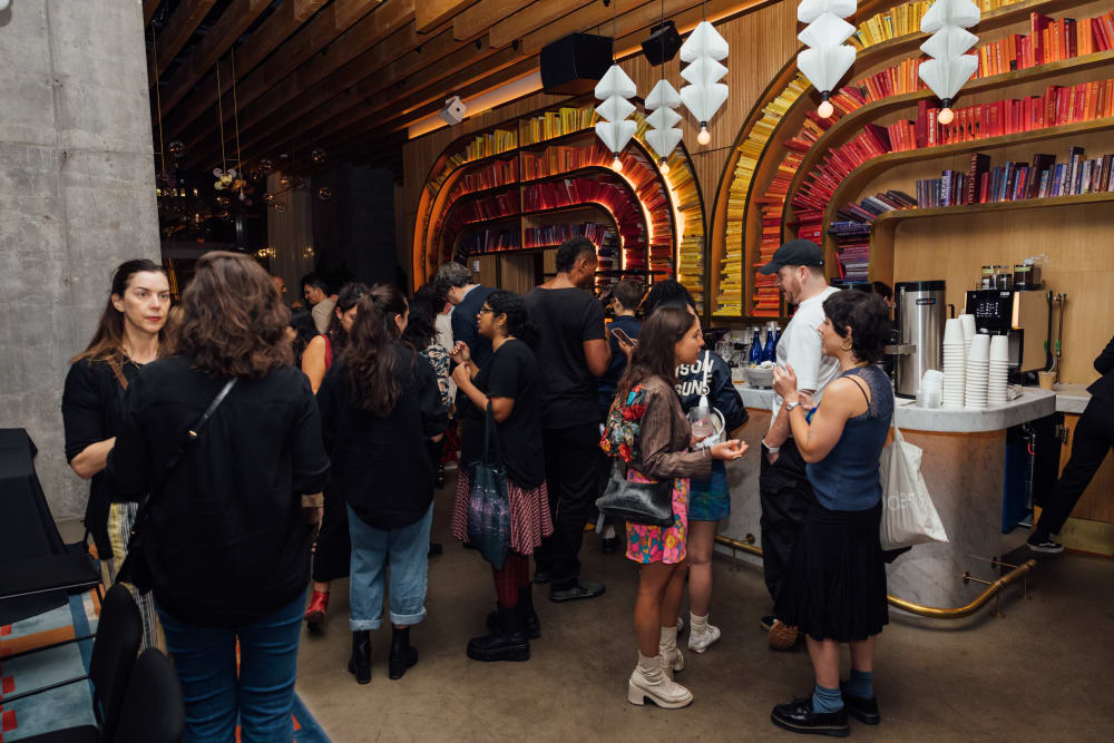 Guests standing at the bar. The wall behind the bar is wood panelled with colour coordinated bookshelves that curve around. 