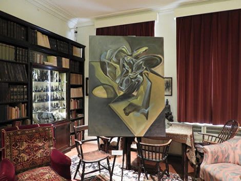 A large abstract painting in a room with two wooden chairs in front of it.