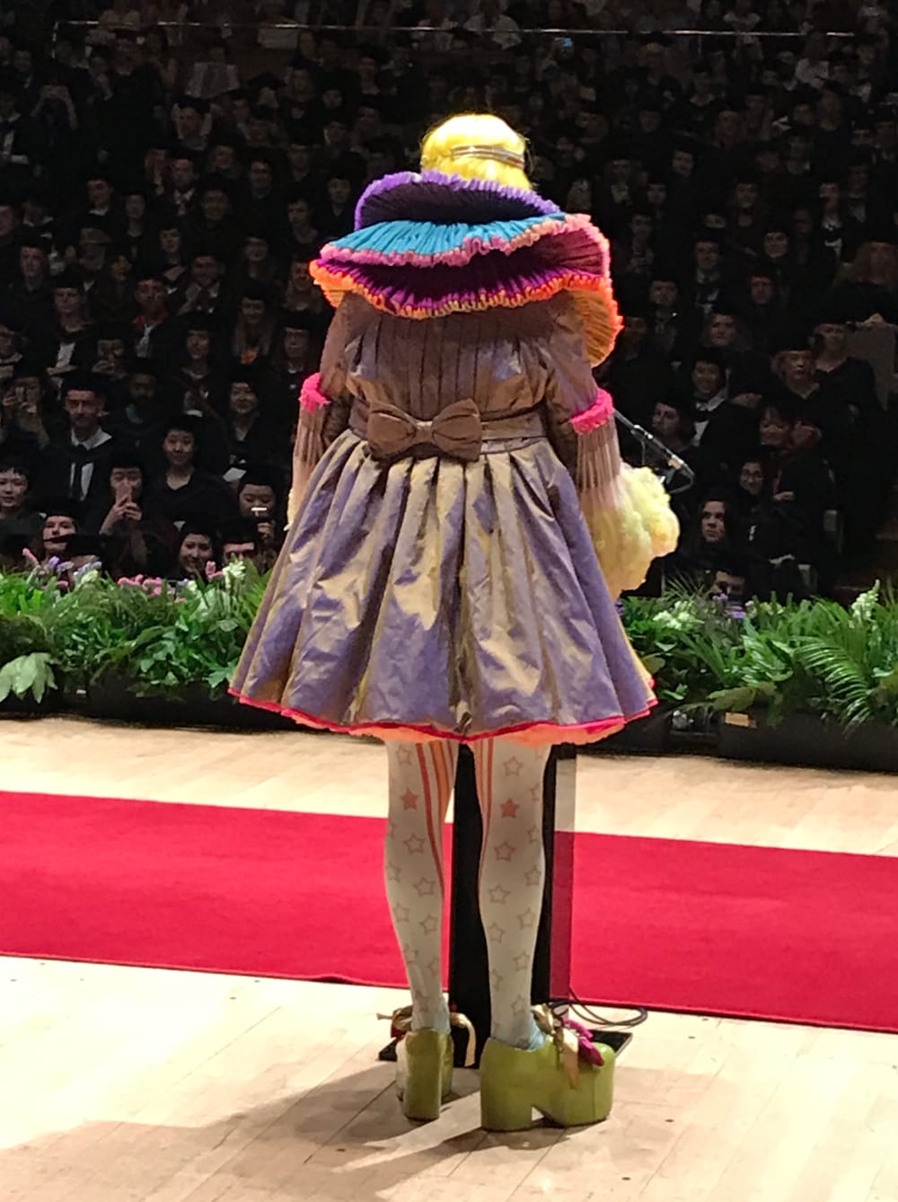 View of Grayson Perry from behind on stage in front of graduation students in audience