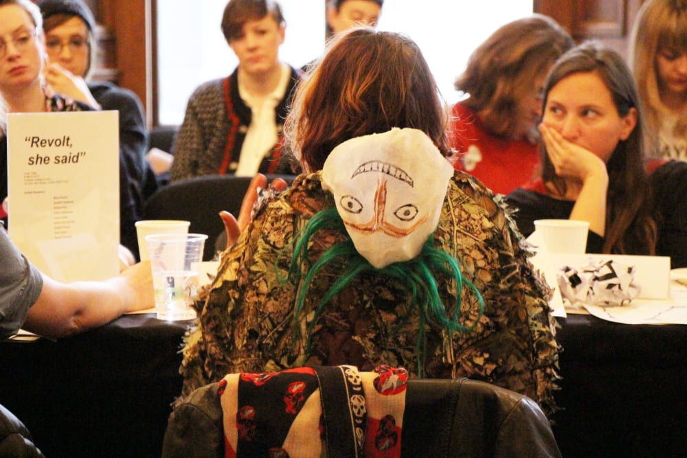 costume of speaker, facing away, pictured seated at the long table discussion