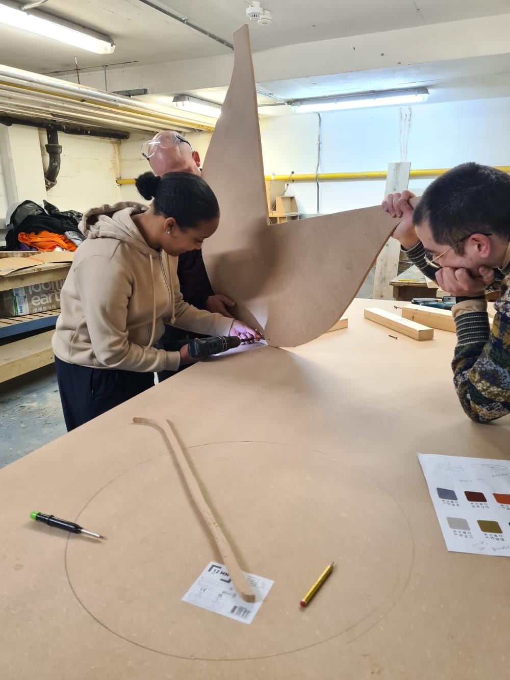 Two men and a woman working together to create wood furniture using wood and drill