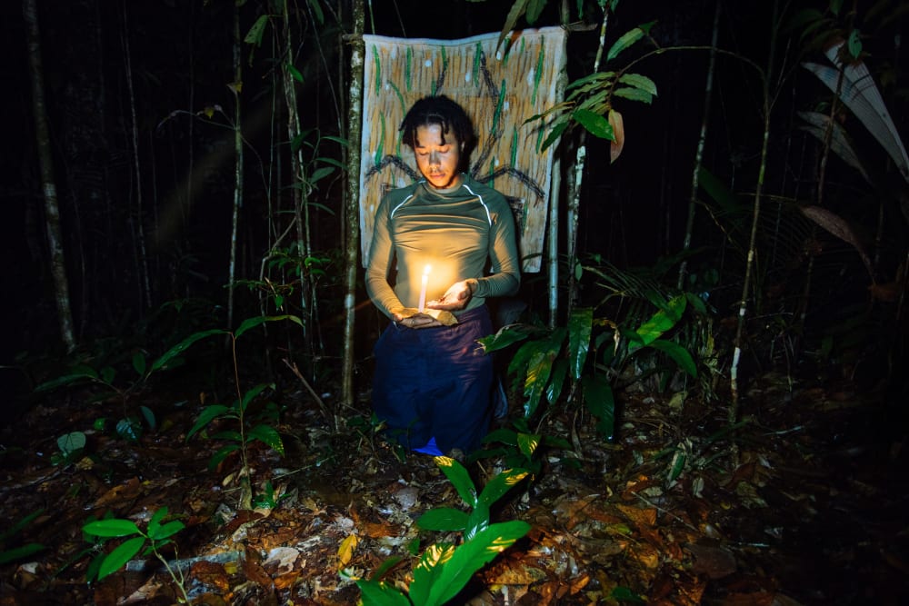 Photograph of Rudy Loewe in Amazonia at night with a candle, talking with an arachnid. 
