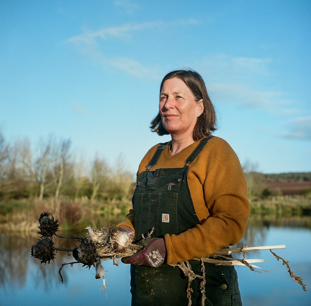 Paula is standing holding reeds. Behind her is a pond and moorland