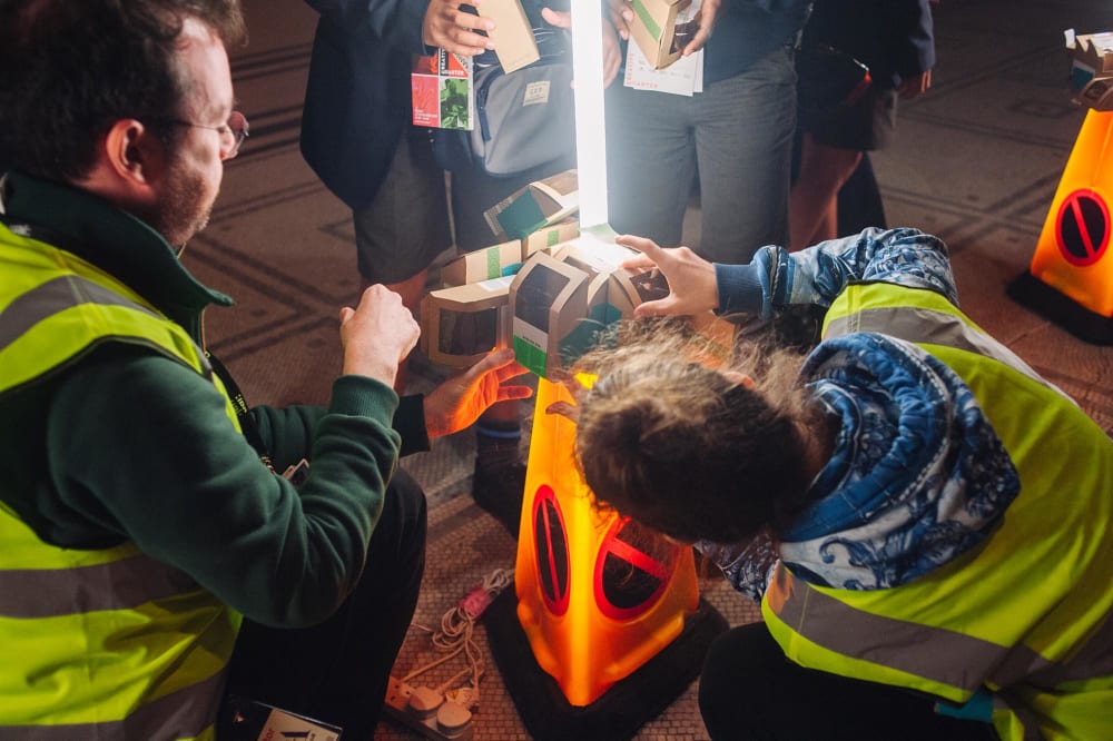A group of students creating a sculpture with cardboard boxes and traffic cones