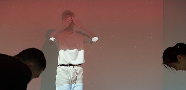 Figure all in white wearing a white mask covering their eyes with their hands.