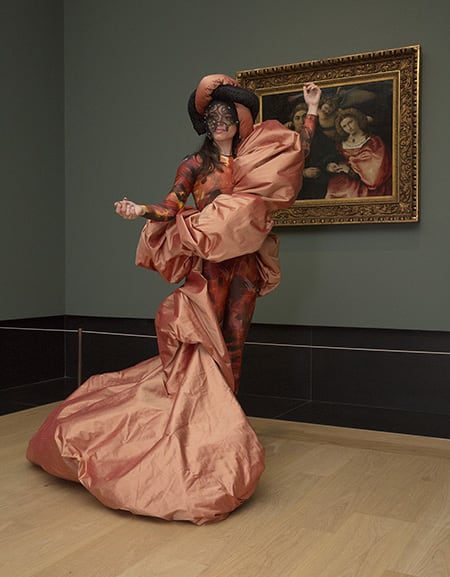 A figure modelling a dress standing in front of a painting.