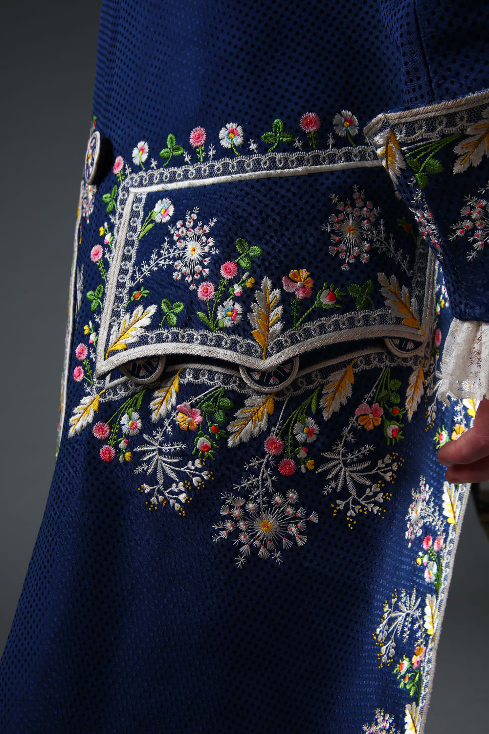 Detail shot showing a pocket with complex floral embroideryin white, pink, green and yellow on blue silk.