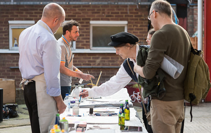 Photo of a group of people at a table outside using paintbrushes