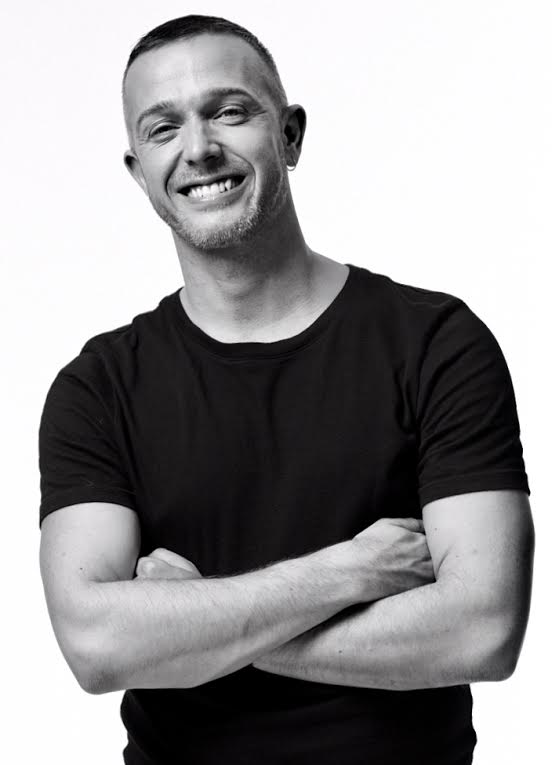 Black and white photo of Patrick Mackie in a black t-shirt smiling to the camera