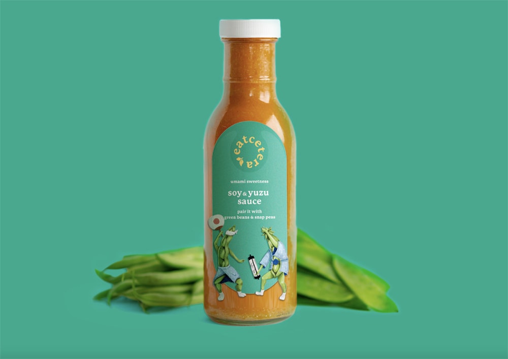 An orange sauce bottle surrounded by edamame pods.