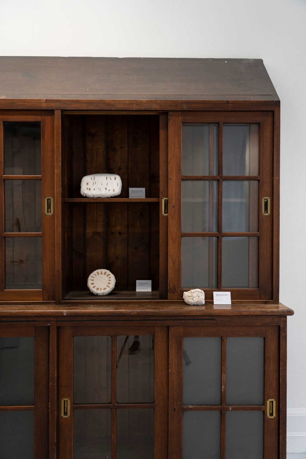 An antique-style wooden cabinet with glass doors displays 3 small white sculptures.