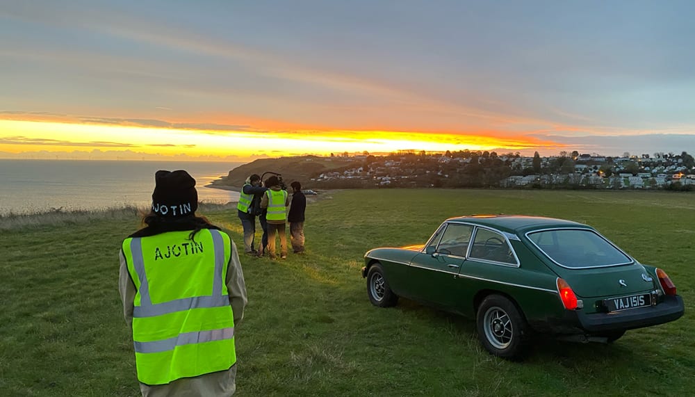 Students wearing high-vis vests film a car on a hilltop.