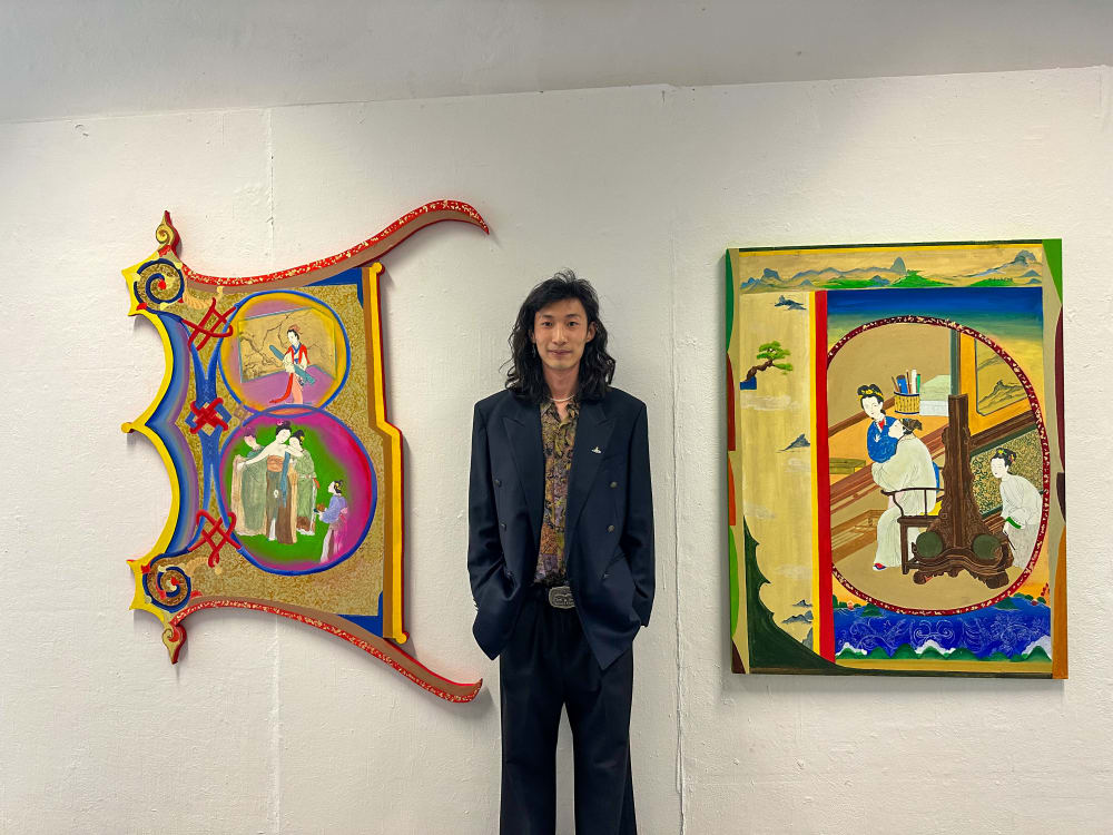 an artist stood in front of two pieces of work displayed on a wall