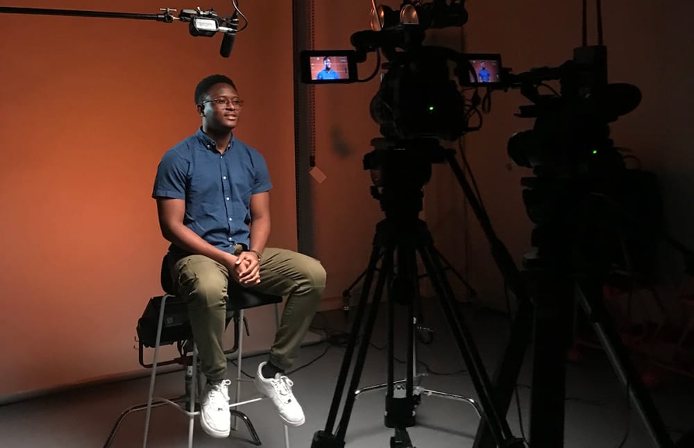 A photograph of someone being interviewed in front of a camera.
