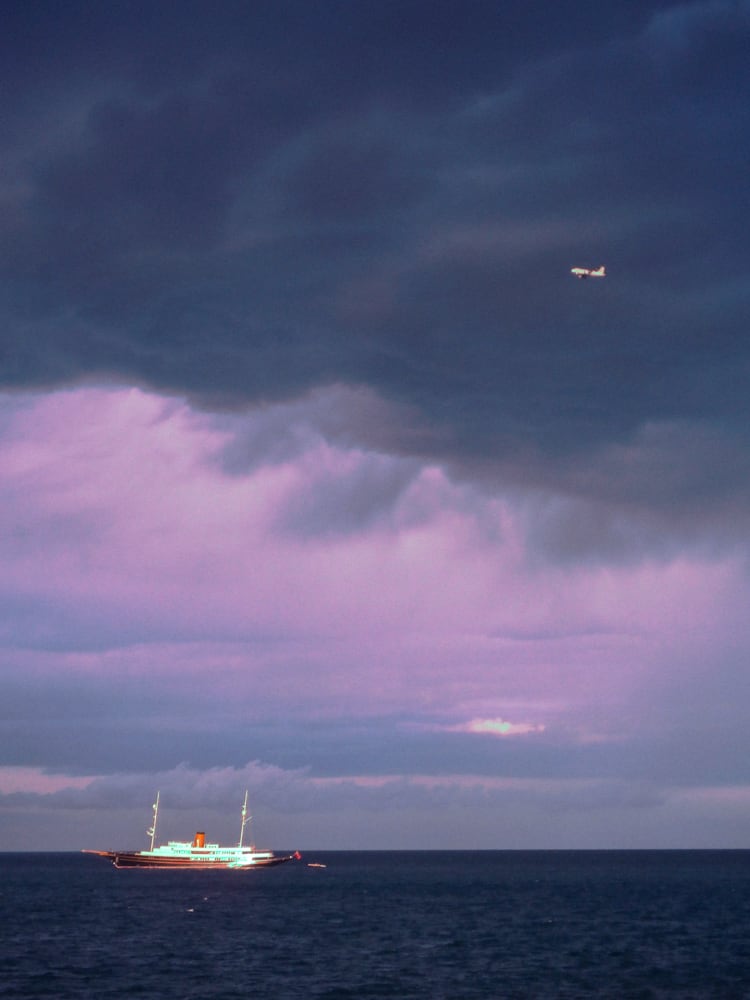A calm seascape with a boat at sea and the horizon in shades of lilac, blue and purple