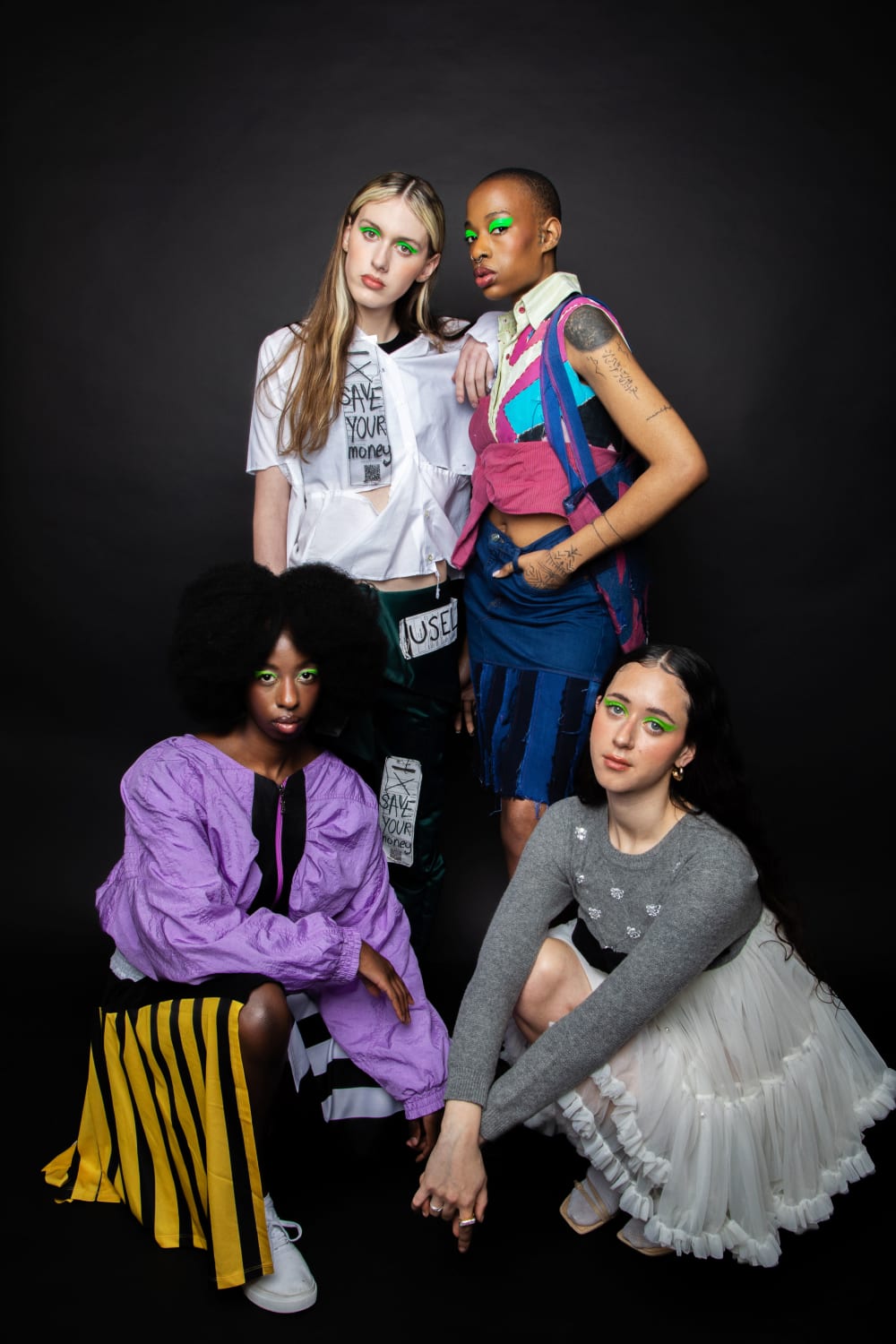 4 models in a studio; 2 standing and 2 crouching. They've all got graphic, neon green eye shadow on. 