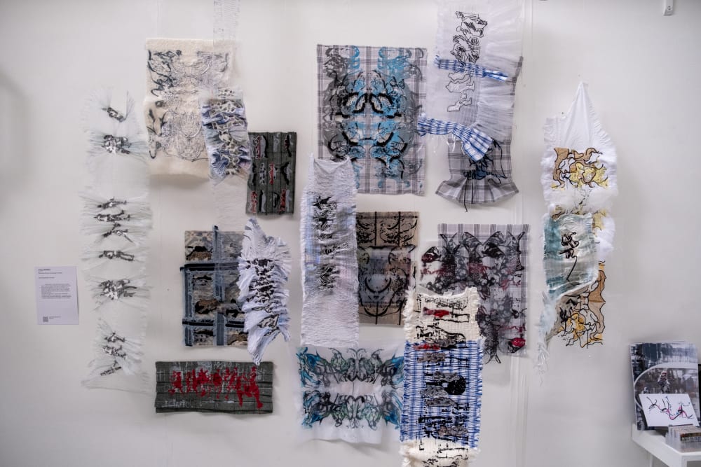 Image shows different coloured and different sized fabrics hanging on a white wall